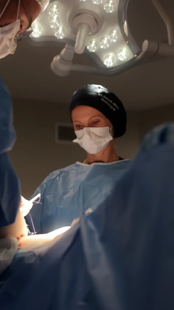 Cirurgiã de touca e máscara sob o foco de luz do centro cirúrgico durante uma cirurgia